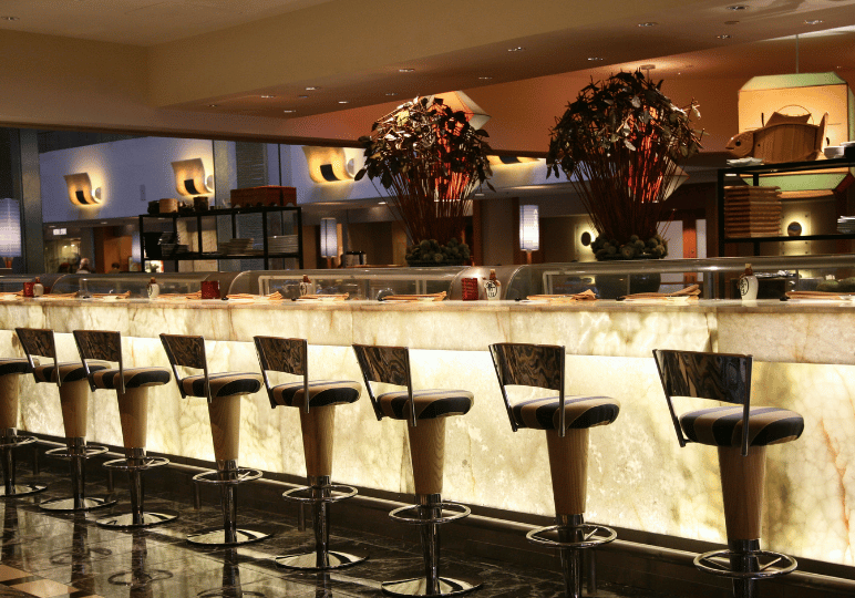 An elegant Japanese restaurant setting featuring a glowing, backlit marble dining counter lined with modern, tall bar stools.