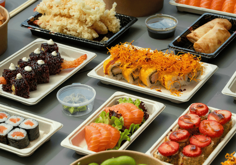 A spread of premium Japanese takeout, including colorful sushi rolls, fresh sashimi, and tempura, neatly arranged in modern, eco-friendly disposable containers.
