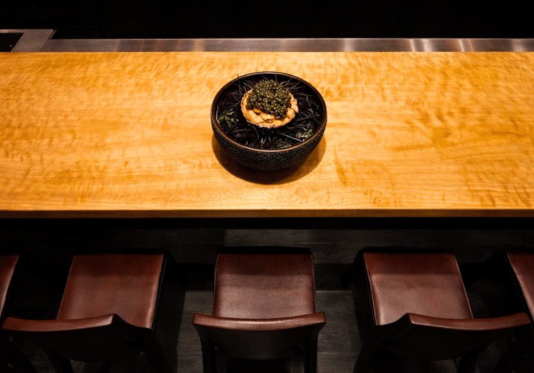 finedining-sg- (2) A beautifully plated luxury dish topped with caviar, centered on a pristine wooden omakase-style counter with dark leather seating.
