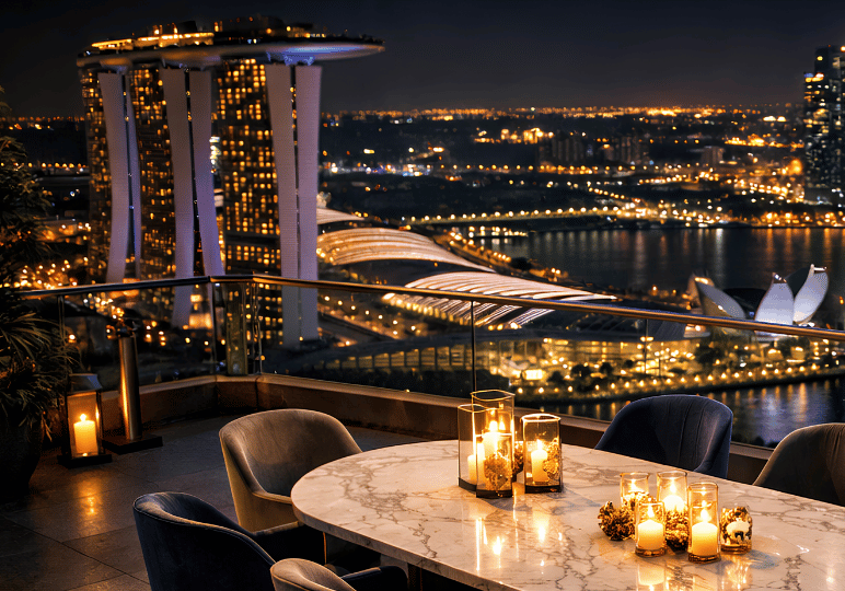 finedining-sg- (3) An exclusive outdoor dining table elegantly set with glowing candles, offering a spectacular nighttime view of the Marina Bay Sands and the glittering Singapore skyline.