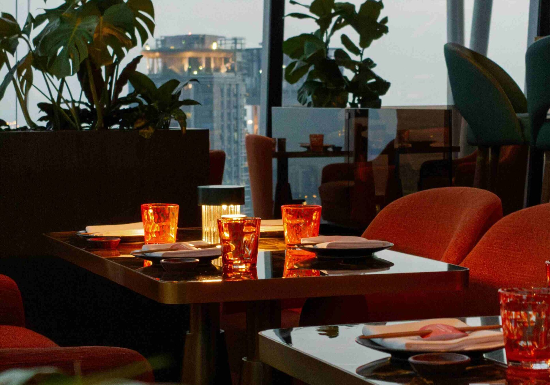 Upscale Singapore rooftop restaurant or bar with vibrant orange chairs and cityscape views at dusk, showcasing fine dining ambiance.