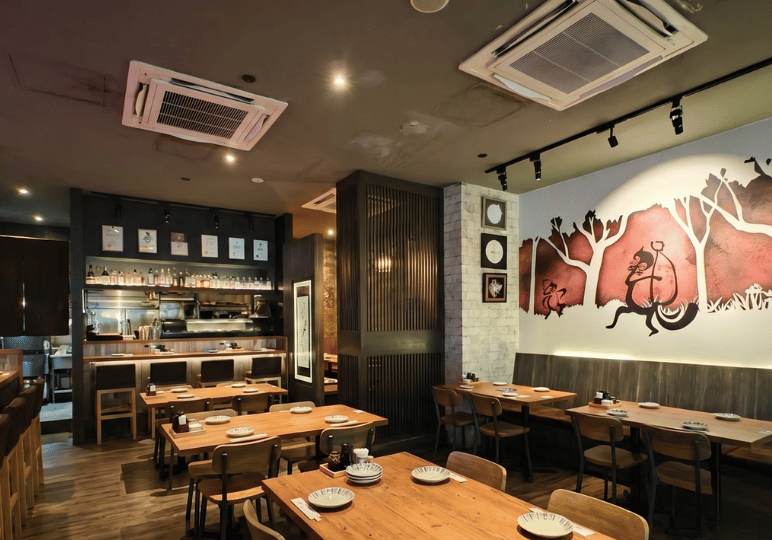 shunjuu-review- (1) Warmly lit dining room at Shunjuu Izakaya featuring wooden tables and a large mural of a monkey on the wall.